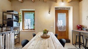 A rustic dining area with a wooden table, chairs, and a kitchen area with a toaster and utensils.