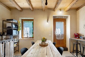 A rustic dining area with a wooden table, chairs, and a kitchen area with a toaster and utensils.