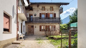 A traditional stone building with a balcony, a gravel courtyard, and a mountain in the background.