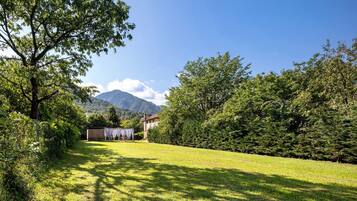 A grassy outdoor area with a building and trees, a mountain in the background, and a clear sky.
