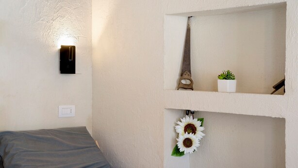 A bedroom with a bed, a wall-mounted light, a mirror, a small plant, and a decorative item.