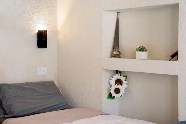 A bedroom with a bed, a wall-mounted light, a mirror, a small plant, and a decorative item.