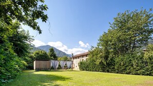 A grassy outdoor area with a stone building, trees, and mountains in the background.