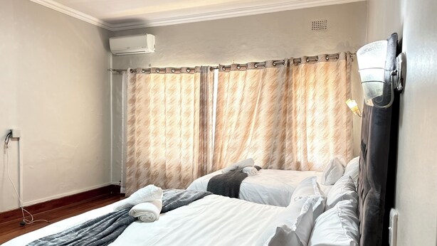 Habitación de hotel con dos camas, una ventana con cortinas, un equipo de aire acondicionado y un enchufe en la pared.