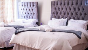 Habitación de hotel con dos camas, cada una con un cabecero capitonado, ropa de cama blanca y una toalla doblada con cuidado.
