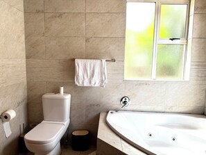 Ein Badezimmer mit Toilette, Waschbecken, Badewanne, einem Fenster mit Milchglas und einem Handtuchhalter.
