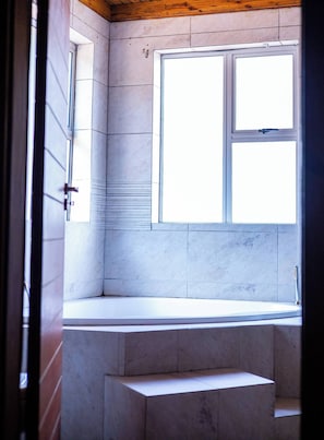 A bathroom with a window, a bathtub, and a shower area. - Room-luxurious Ensuite - A (Johannesburg)