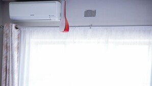Ein Hotelzimmer mit Bett, Kissen, einem Fenster mit Vorhängen und einer Klimaanlage.