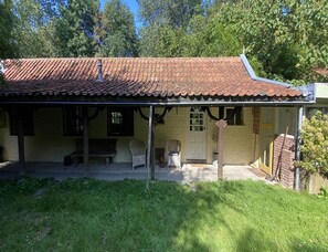Ein eingeschossiges Gebäude mit einem Ziegeldach, einer Veranda mit Sitzgelegenheiten und einer Tür.