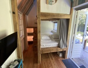 Ein Schlafraum mit Etagenbetten, einem Fernseher, Holzboden und einer Tür, die nach draußen führt.