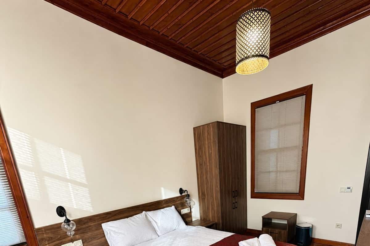 Una habitación de hotel con cama, sofá, armario, ventana y lámpara colgante.