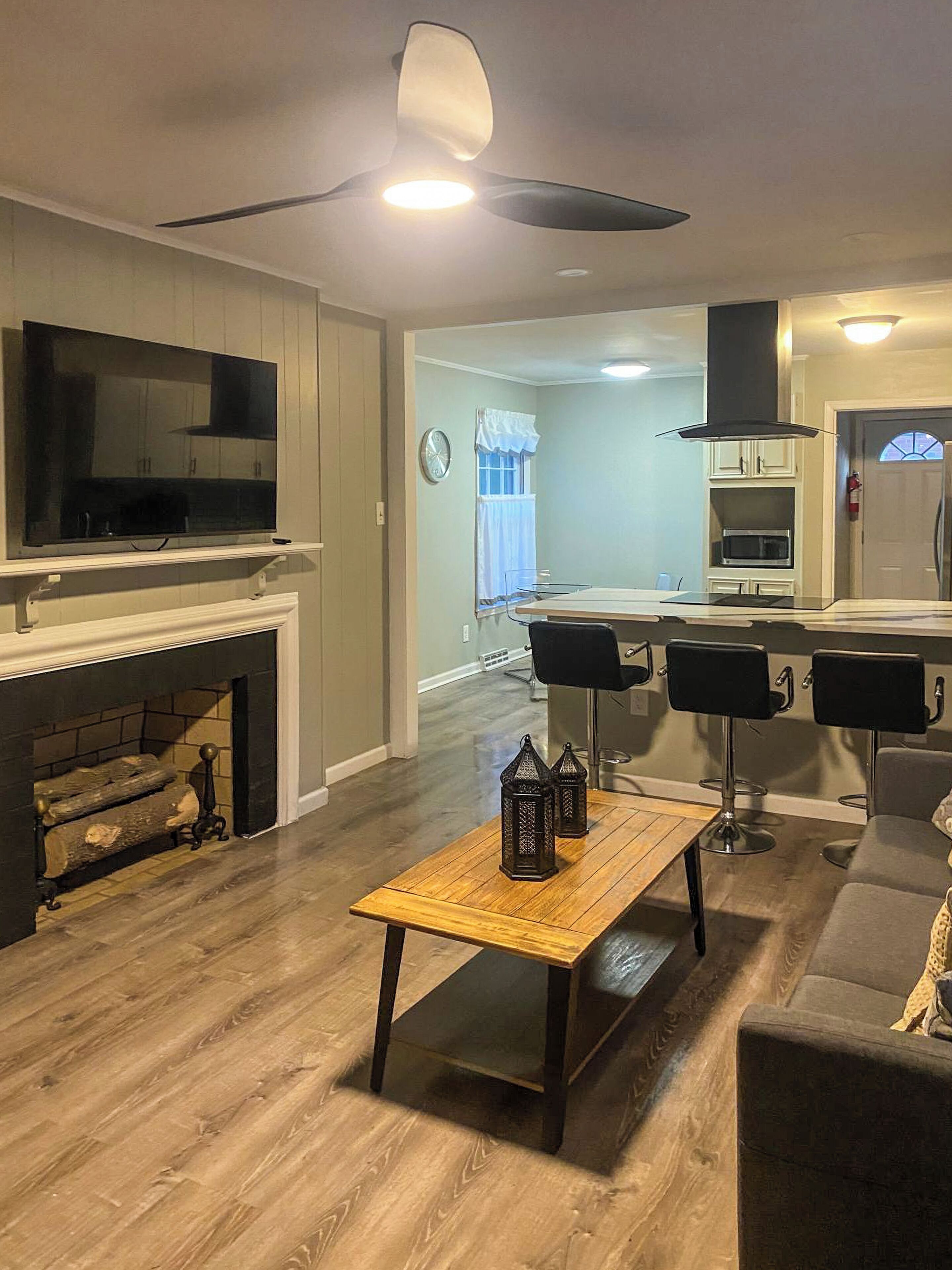 Una sala de estar moderna con chimenea, televisor y una zona de comedor con taburetes de bar.