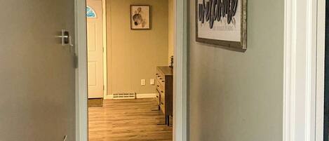 A hallway with a wooden floor leading to a room with a door and a framed welcome sign.