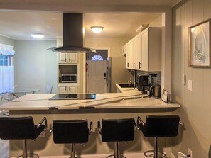 Una cocina moderna con una isla central, taburetes de bar, microondas y refrigerador.