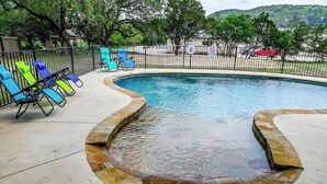 A swimming pool with a stone edge, surrounded by a fence, and several lounge chairs. - Highlife - Sleeps 23 - Frio River Access w/ Private Pool & Outdoor Kitchen (Concan)