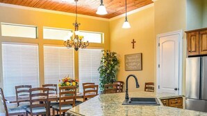 A kitchen with a granite countertop, wooden cabinets, a stainless steel refrigerator, and a dining area with wooden chairs and a chandelier. - Highlife - Sleeps 23 - Frio River Access w/ Private Pool & Outdoor Kitchen (Concan)