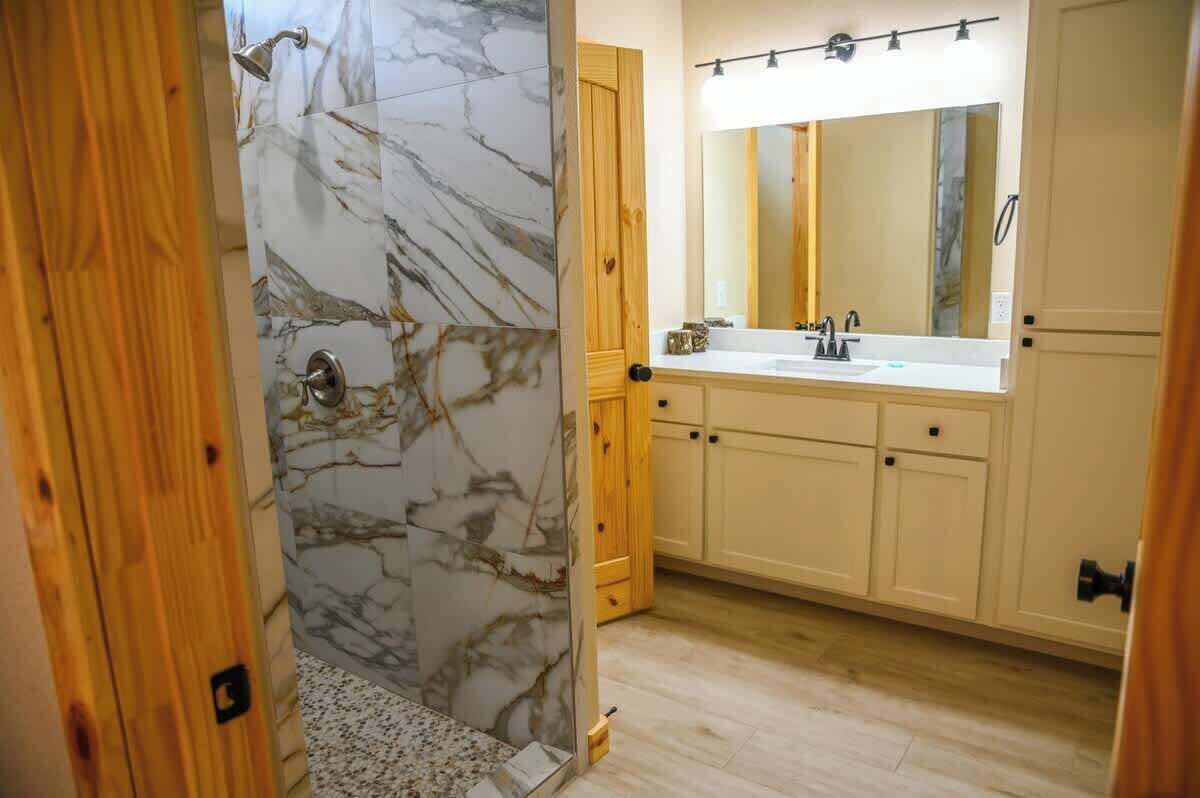 A bathroom with a marble shower wall, a sink with a mirror, and wooden cabinets.