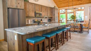 Een keuken met houten kasten, een roestvrijstalen koelkast, een marmeren aanrecht en een bar met krukken.