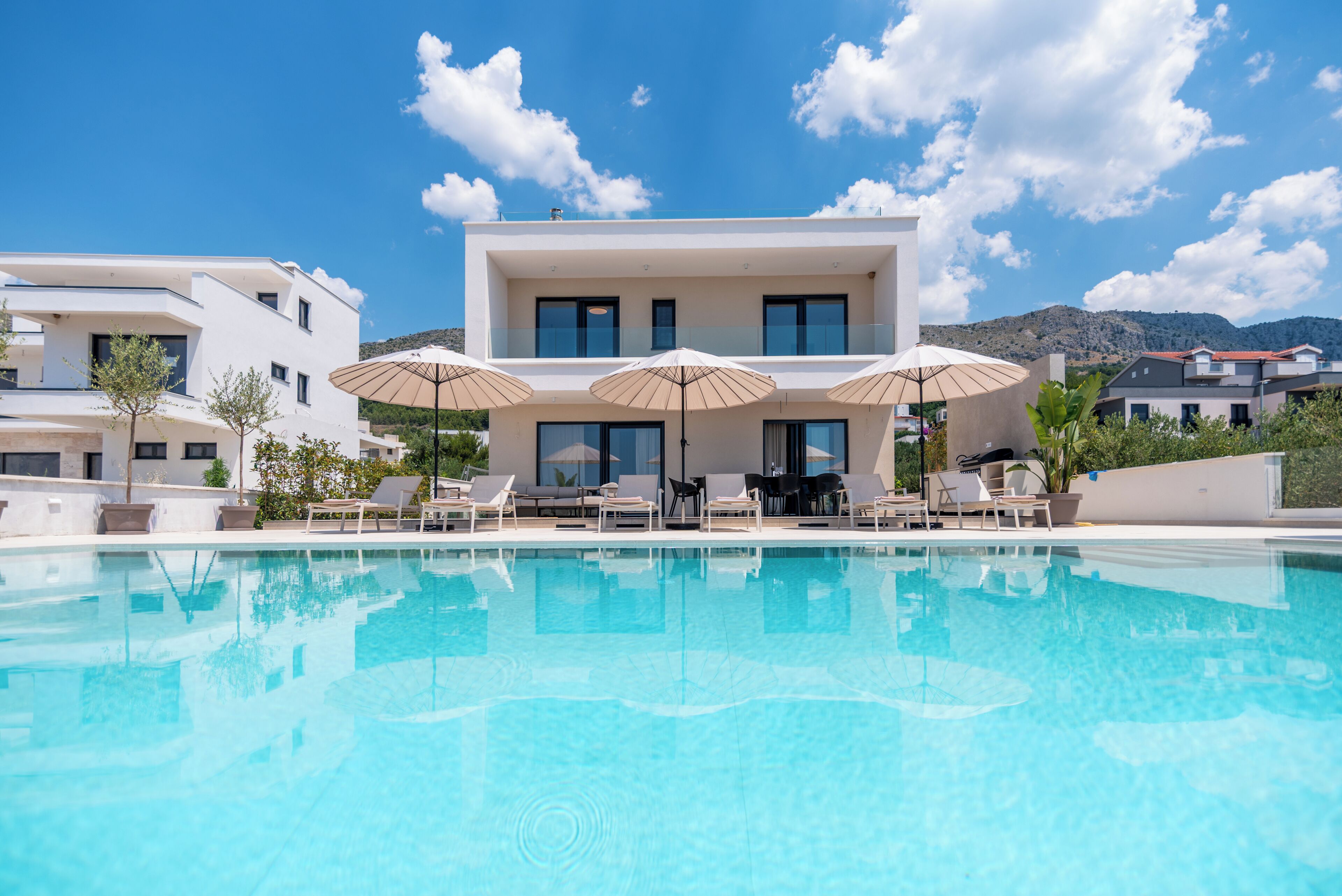 A modern hotel with a pool, lounge chairs, and umbrellas.
