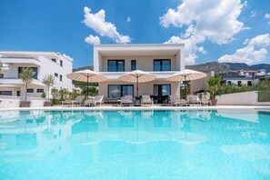 Um hotel moderno com piscina, espreguiçadeiras e guarda-sóis.