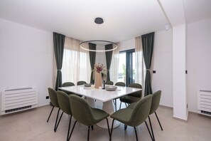 A modern dining room with a round table, six chairs, a vase with flowers, and a pendant light. - Exclusive new villa W H pool overlooking Split & Sea (Podstrana - Sv. Martin)