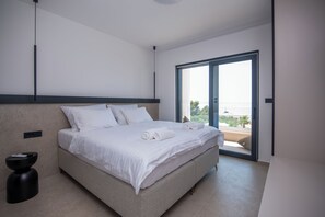 A modern hotel room with a large bed, a small side table, and a sliding glass door leading to a balcony. - Exclusive new villa W H pool overlooking Split & Sea (Podstrana - Sv. Martin)