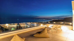 Una terraza en la azotea con vistas despejadas al mar, barandilla de cristal y mobiliario moderno para exteriores.