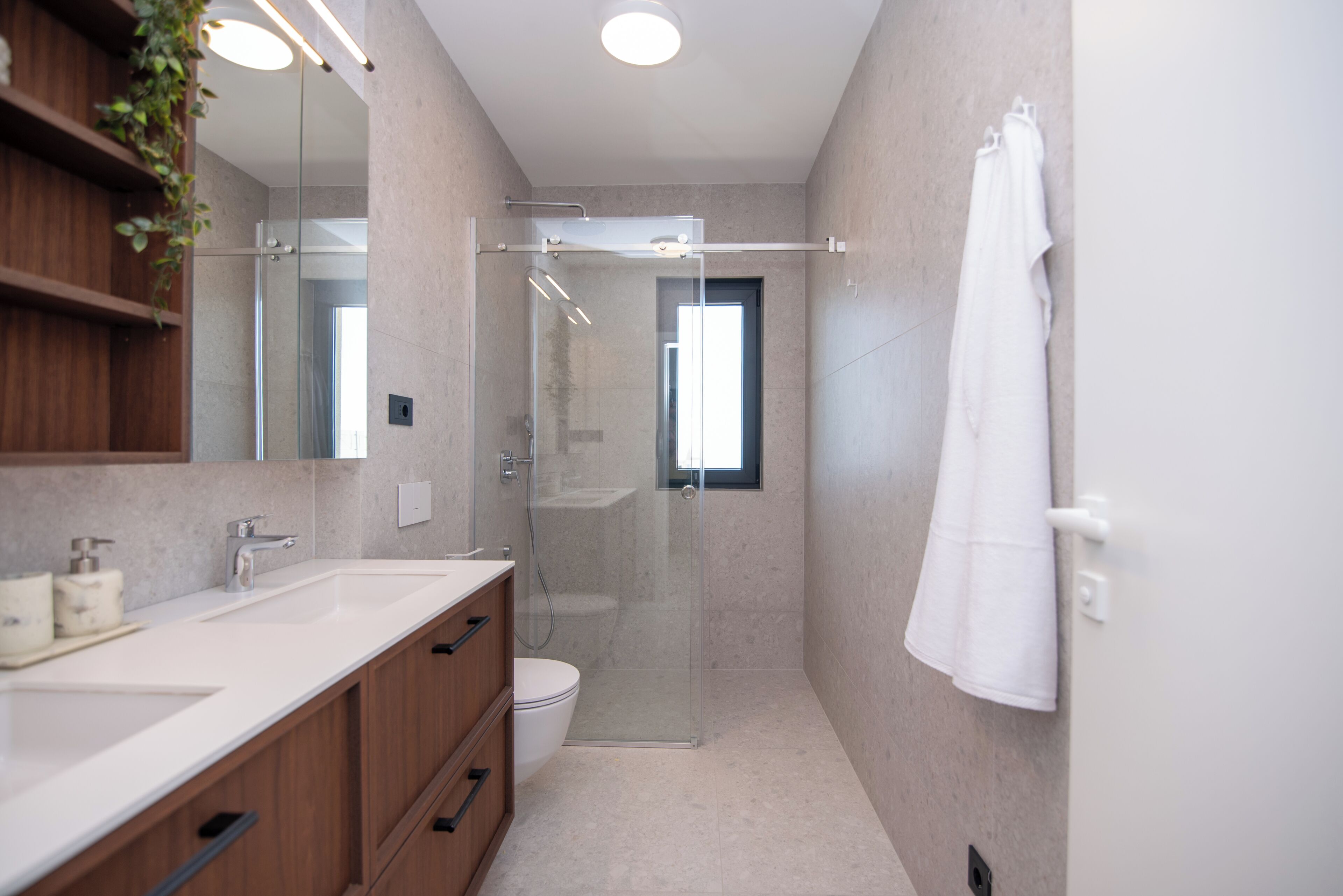 A modern bathroom with a glass-enclosed shower, a white toilet, and a wooden vanity with a mirror.