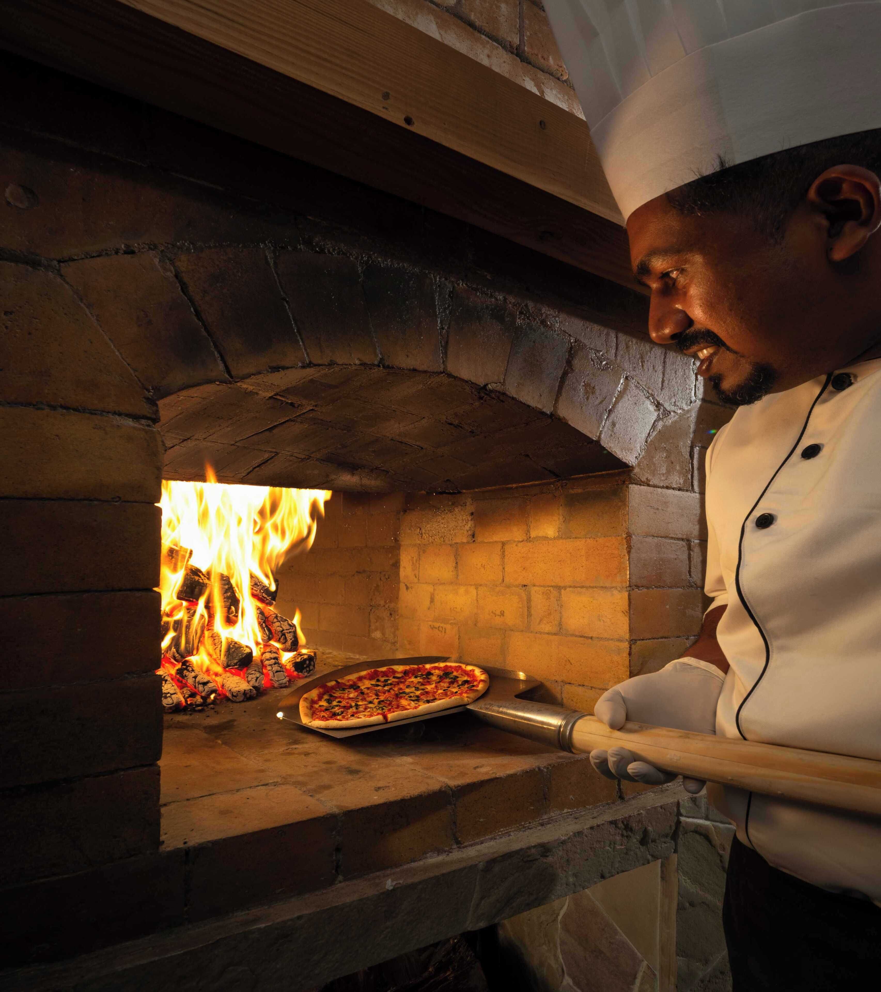 Un chef prépare une pizza dans un four en briques.