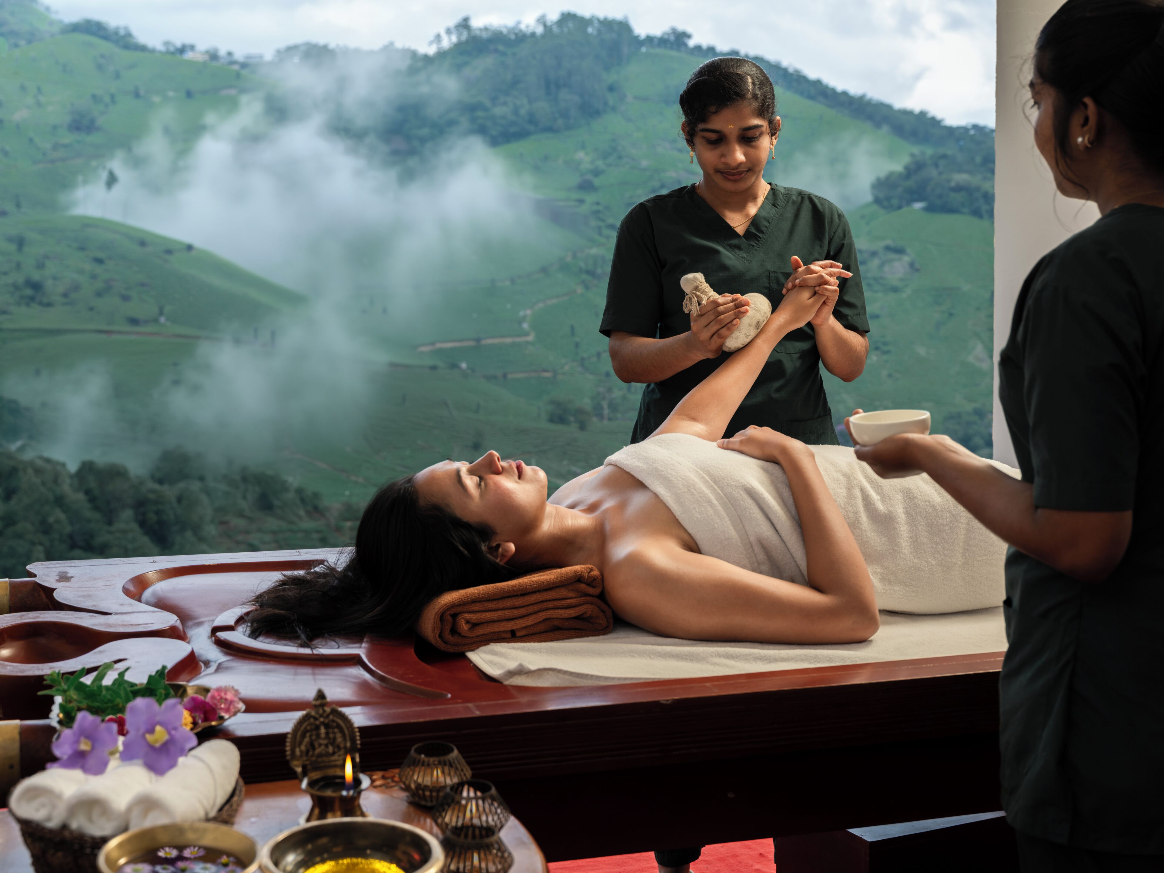A massage therapy session with a scenic view of green hills and mist in the background.