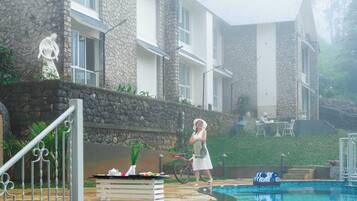 A poolside area with a stone building, a dining table with food, and a person near the pool.