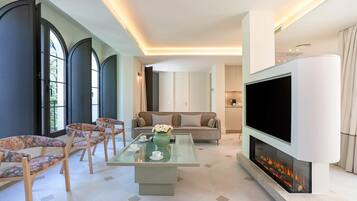 A modern living room with a glass coffee table, sofas, a flat-screen TV, and a fireplace.