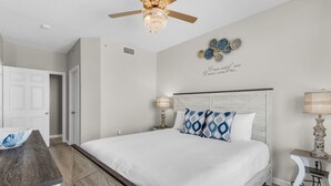 Un dormitorio con cama, mesitas de noche, ventilador de techo y un adorno en la pared.