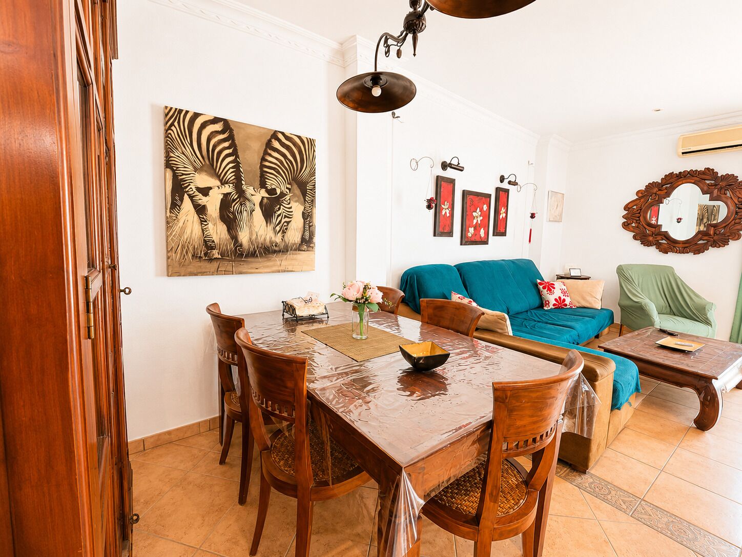 A dining area with a wooden table and chairs, a blue sofa, and a zebra-themed painting on the wall.