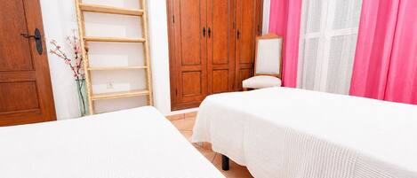 A bedroom with two beds, wooden wardrobe, and a window with pink curtains.