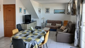 Un salon comprenant un canapé, un téléviseur, une table à manger avec des chaises et un escalier.