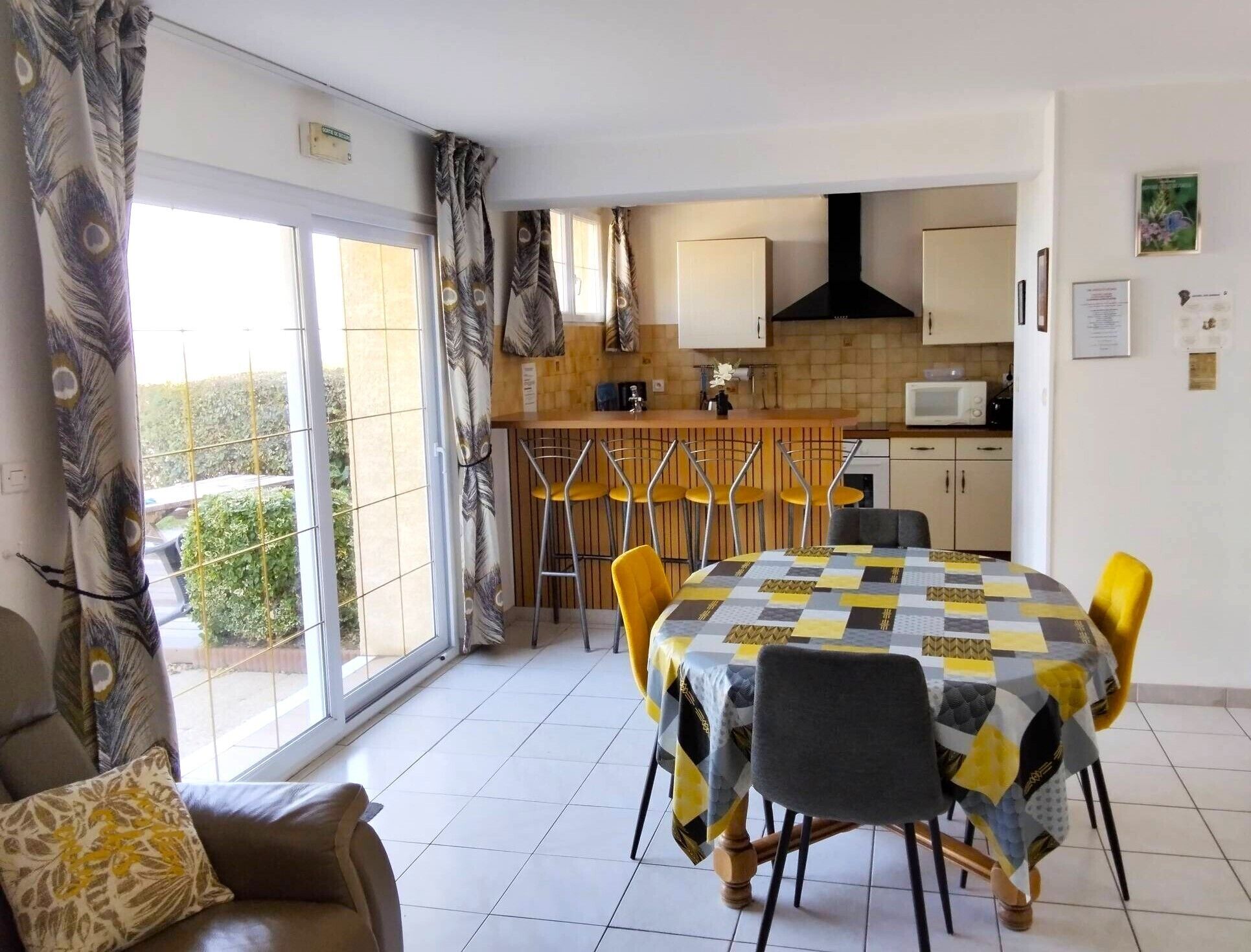 A dining area with a table covered in a checkered tablecloth, yellow chairs, and a sofa with a patterned cushion.