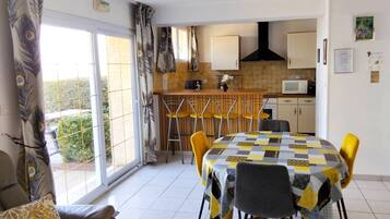 A dining area with a table covered in a checkered tablecloth, yellow chairs, and a sofa with a patterned cushion.