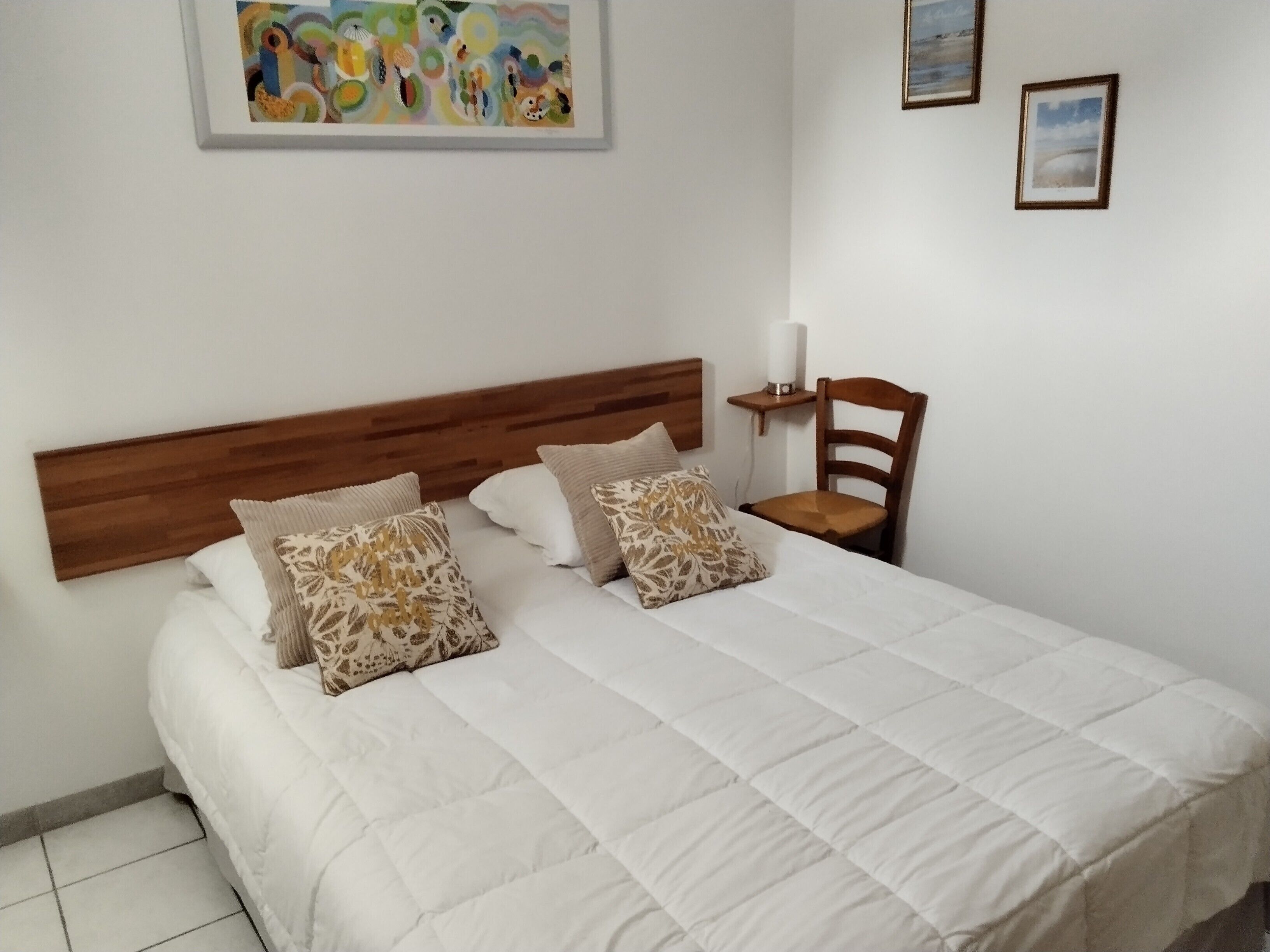 A neatly made bed with a wooden headboard, two pillows, a bedside table with a lamp, and a chair.