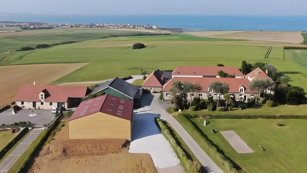 Vue aérienne d’un quartier résidentiel avec des maisons, un grand champ ouvert et une étendue d’eau au loin.