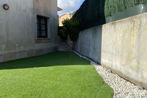 A narrow courtyard with artificial green turf, a concrete wall, and a window.