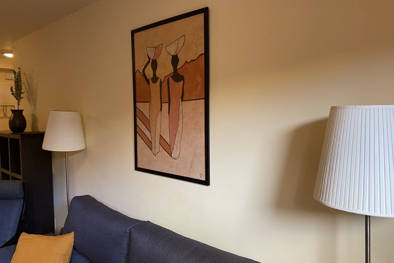 A living room with a sofa, a lamp, and a framed abstract painting on the wall.