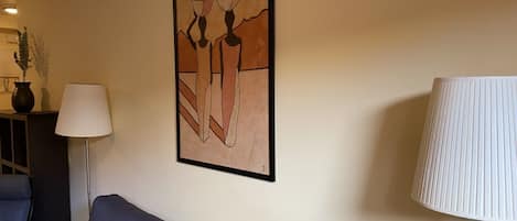 Uma sala de estar com um sofá, uma luminária e um quadro abstrato emoldurado na parede.
