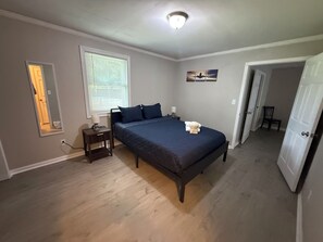 A bedroom with a bed, bedside tables, a window with blinds, a door, and a painting on the wall. - Wanda Way Gorgeous 3-bedroom house with AC in charming Pensacola (Pensacola)
