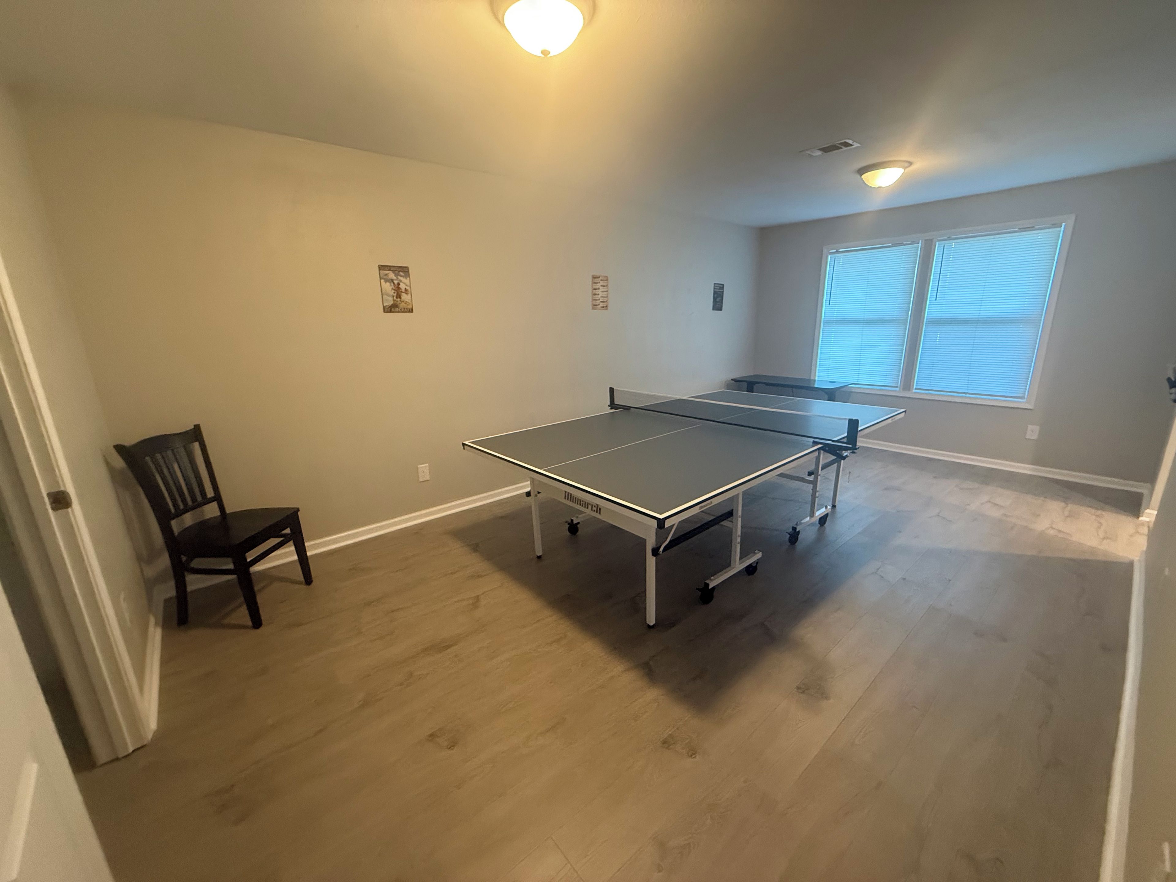 Una stanza con tavolo da ping pong, una sedia e una finestra con tende.