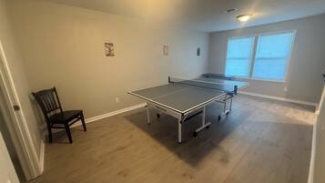 Una stanza con tavolo da ping pong, una sedia e una finestra con tende.