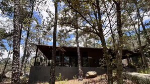 A cabin with a sloped roof, surrounded by trees and rocks, with a clear sky above. - Constanza de GEstores (Huasca De Ocampo)