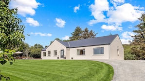 A two-story house with a well-maintained lawn and a gravel driveway. - Owen Glen Cottage Clifden (Clifden)