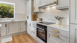 A modern kitchen with white cabinetry, a built-in oven, and a window overlooking greenery. - Owen Glen Cottage Clifden (Clifden)