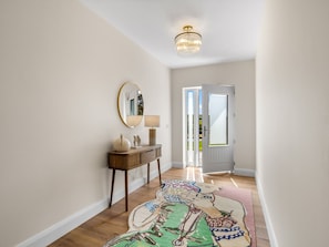 A hallway with a wooden floor, a round mirror, a small table with a lamp, and a colorful rug. - Owen Glen Cottage Modern Holiday Home Near Clifden Town (Clifden)